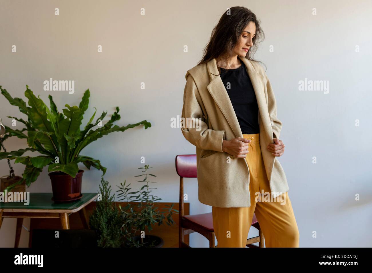 Beautiful female model wearing jacket looking down while standing at home Stock Photo