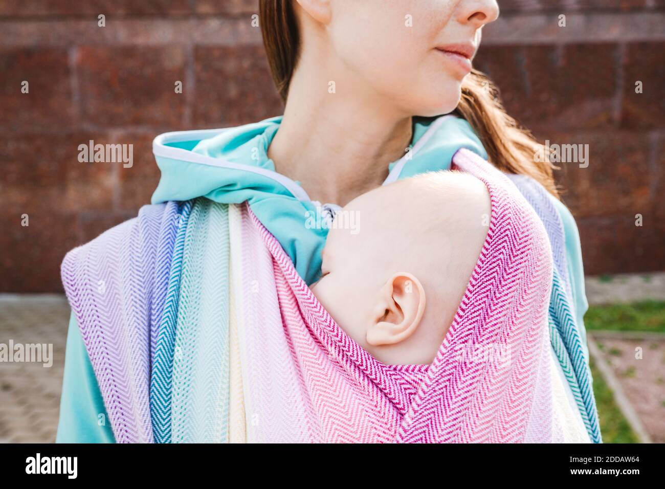 Midsection mother carrying baby wrapped in blanket standing on sunny day Stock Photo