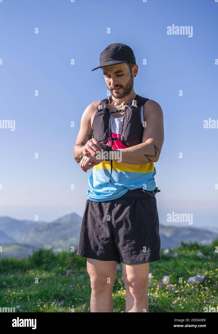 Mid adult man wearing cap and bottle strap checking time on watch while standing on mountain Stock Photo