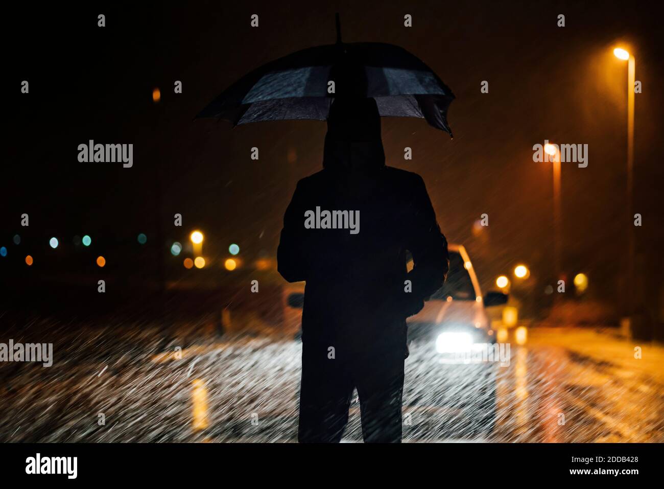 Young man with umbrella standing in front of car dutimng a rainy night Stock Photo