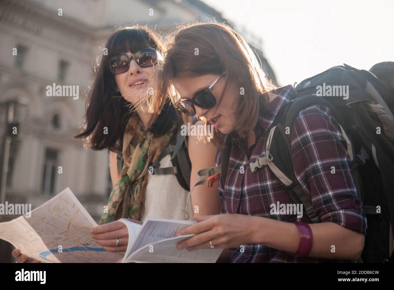 Women on vacation reading map while sitting at town square Stock Photo