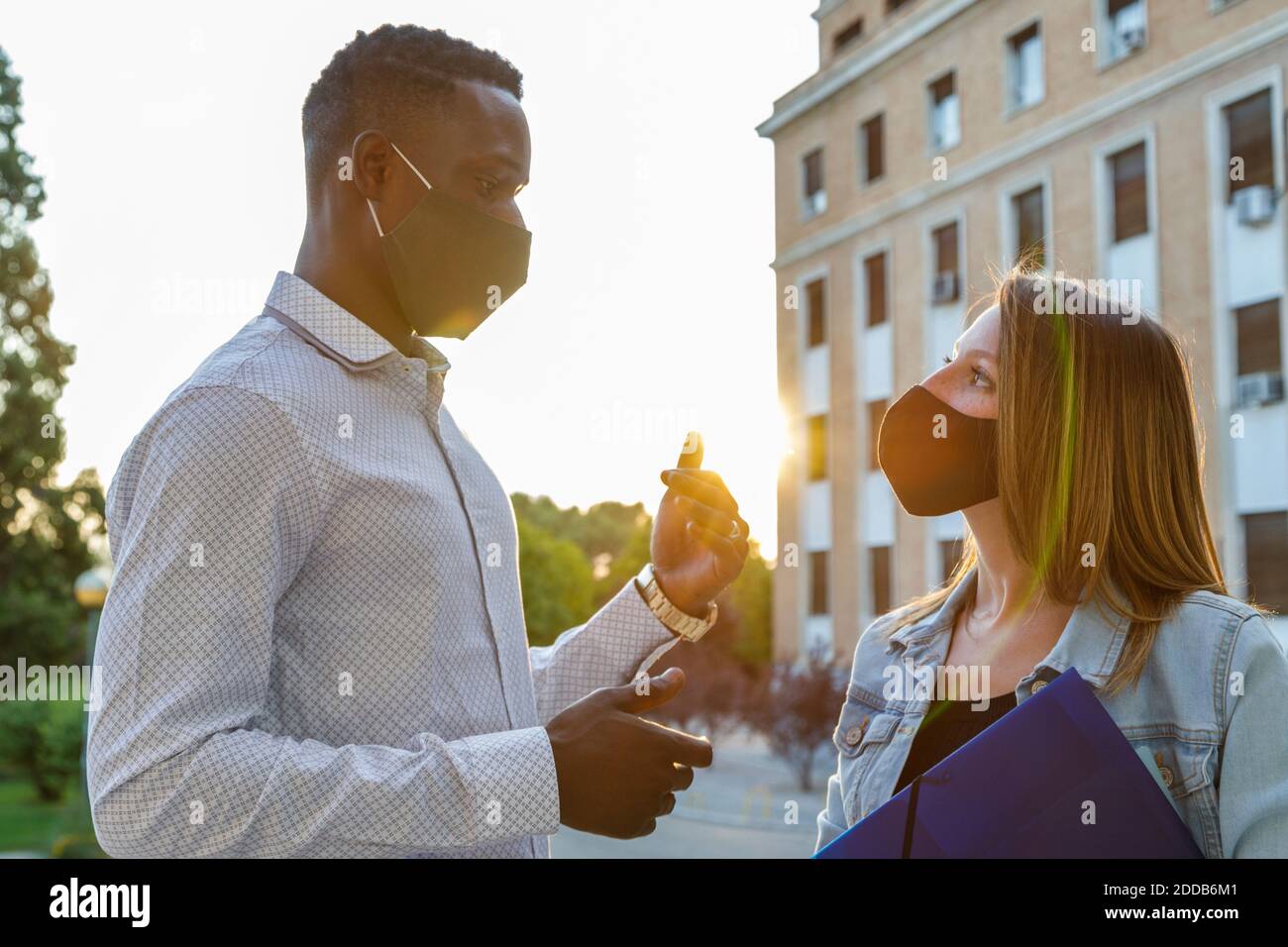Male and female students wearing protective face mask while discussing in university campus Stock Photo