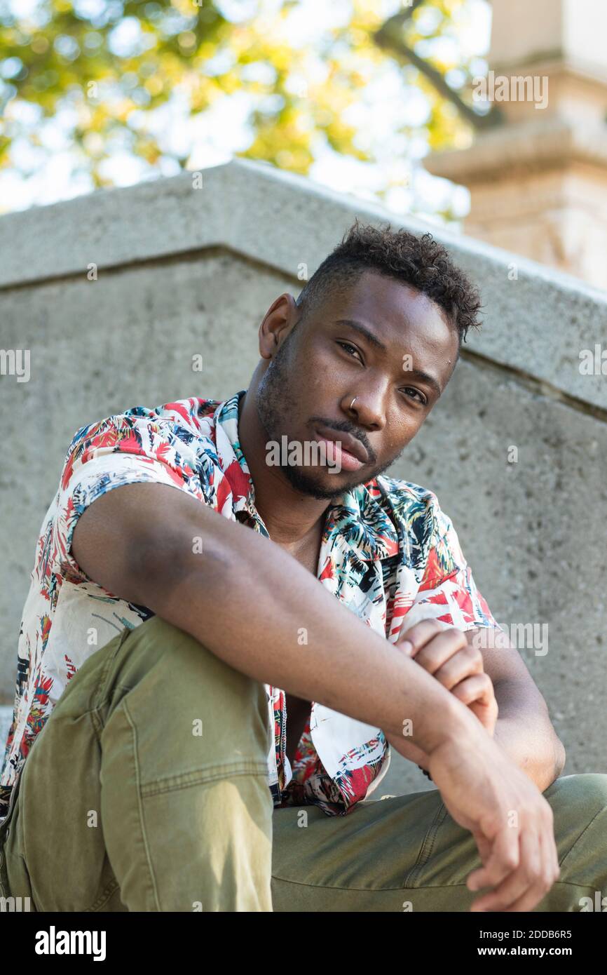 Serious young man sitting by retaining wall Stock Photo