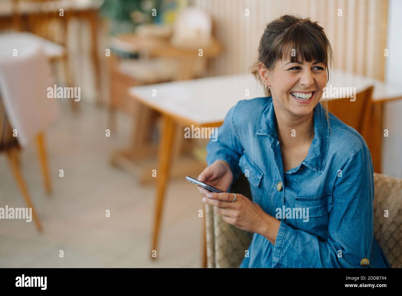 Female owner laughing while using smart phone sitting in cafe Stock ...