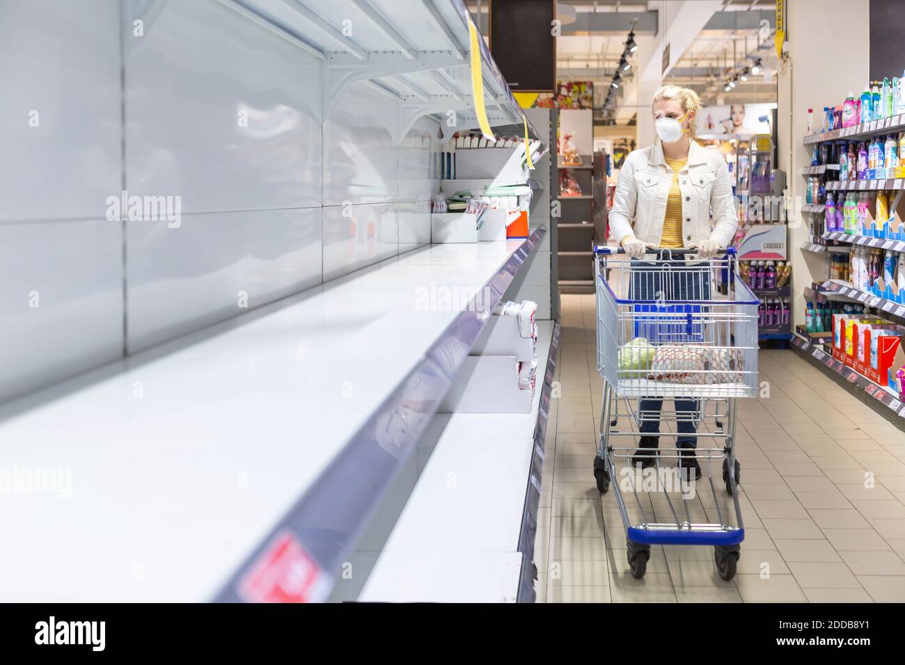 Teenage girl wearing protectice mask and gloves looking at empty shelves at supermarket Stock Photo