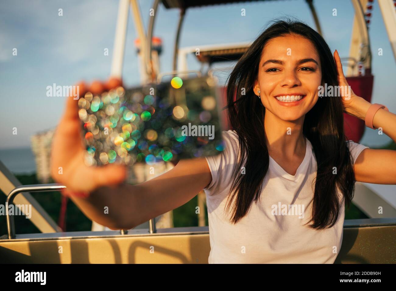 Happy beautiful woman taking selfie with hand in hair on Ferris wheel at amusement park Stock Photo