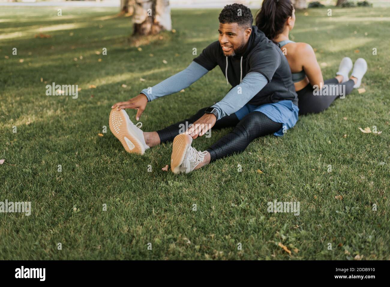 Man touching toes while sitting back to back with woman at backyard Stock Photo