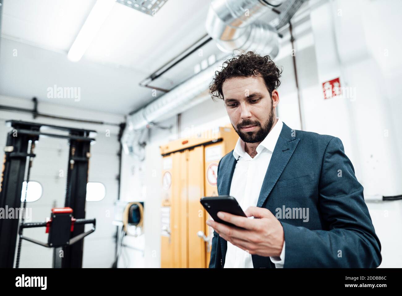 Male engineer using smart phone while standing at industry Stock Photo