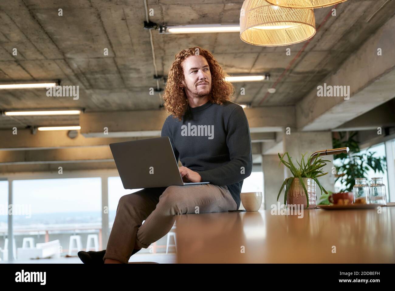 Thoughtful redhead man looking away while using laptop sitting at home Stock Photo