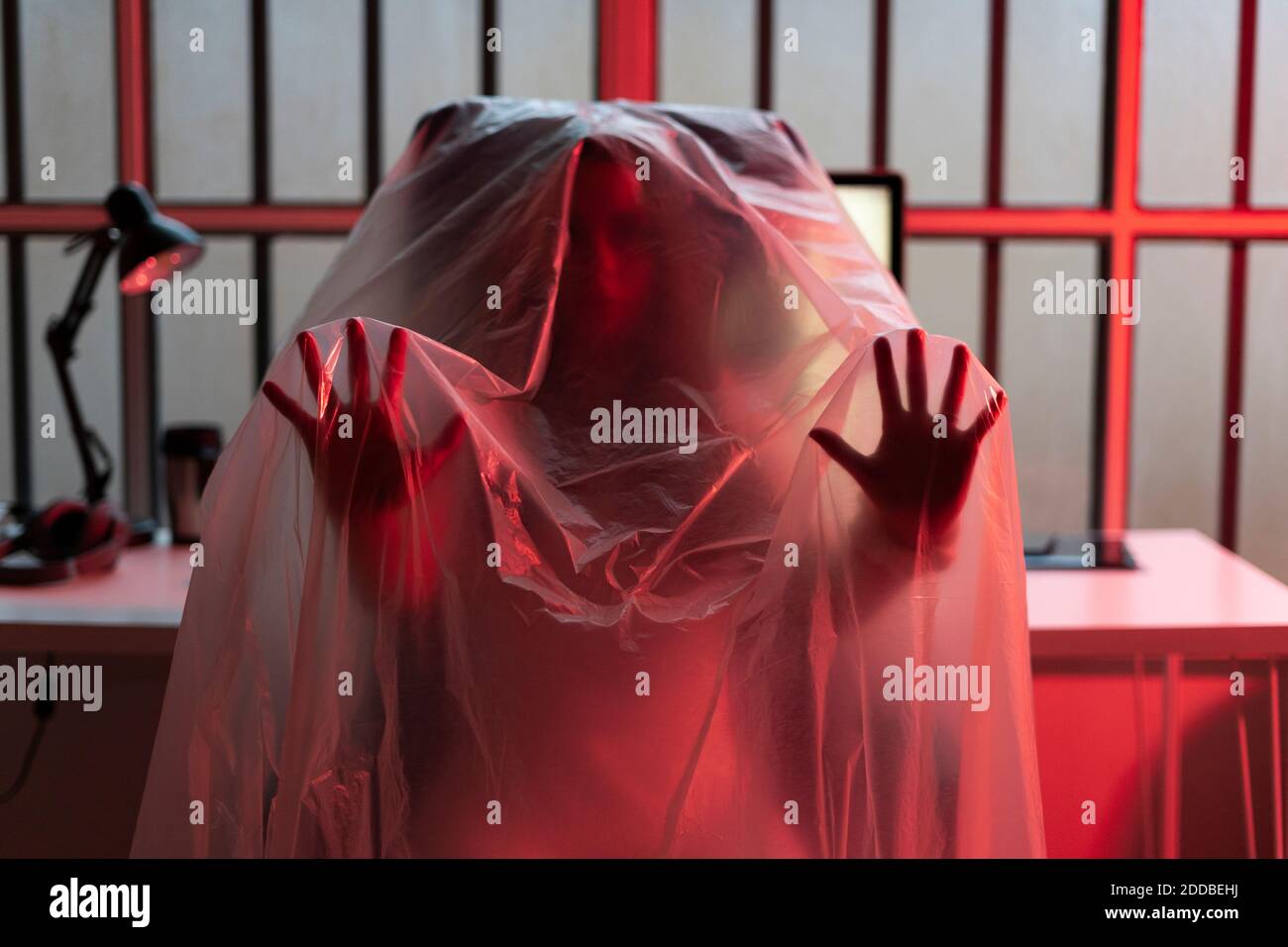 Young woman gesturing while covered with plastic at home office during COVID-19 Stock Photo