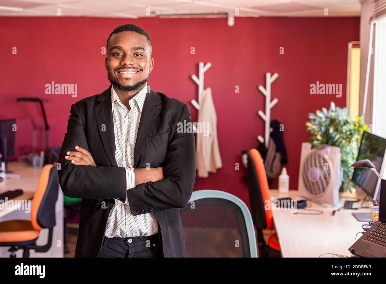 Confident businessman standing with arms crossed in coworking office ...