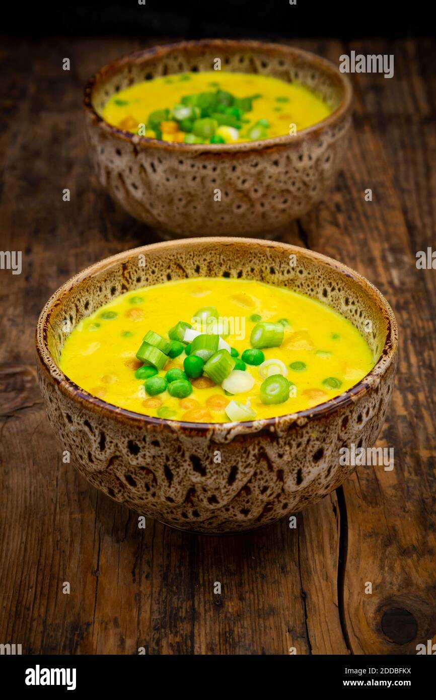Two bowls of vegan coconut soup with green peas, chick-peas, scallion and turmeric Stock Photo