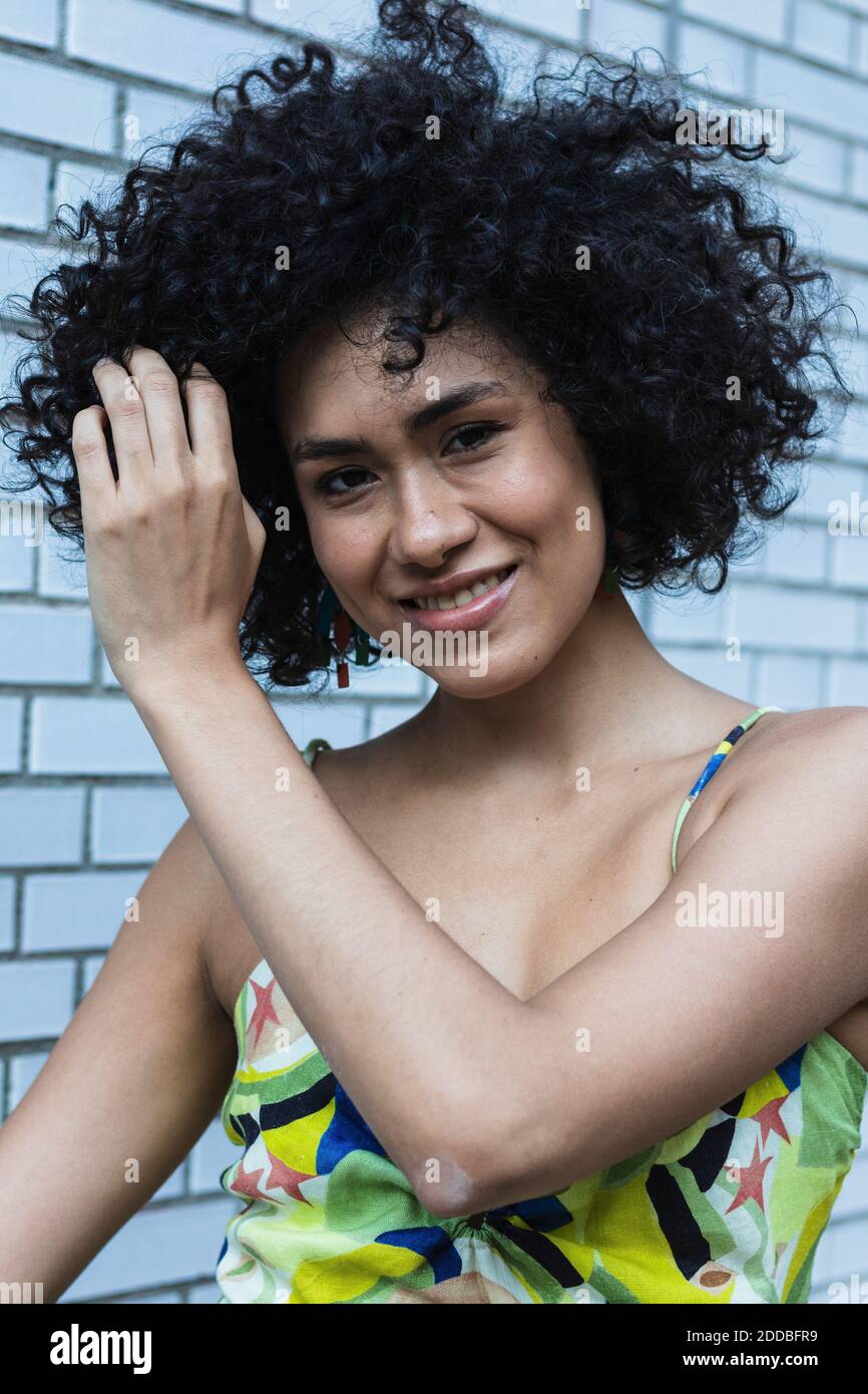 Smiling young woman with hand in hair standing against tiled wall Stock ...