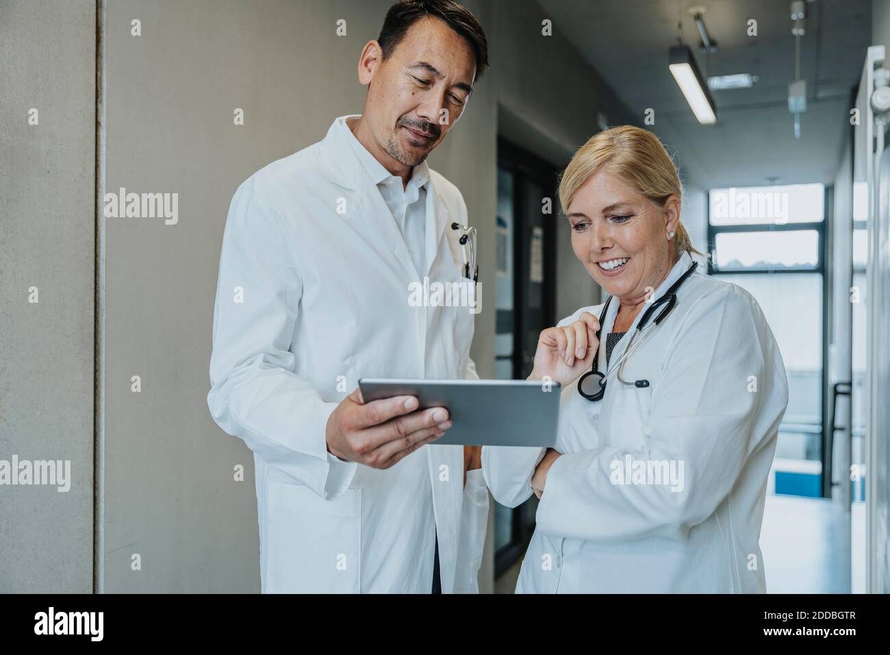 Smiling scientist and doctor using digital tablet while standing at clinic corridor Stock Photo