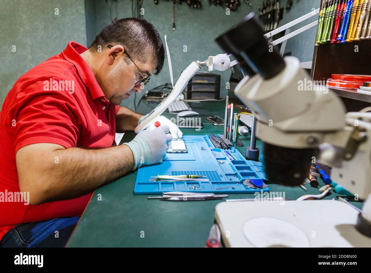 Engineer looking at broken smart phone through magnifying glass in electronics repair shop Stock Photo