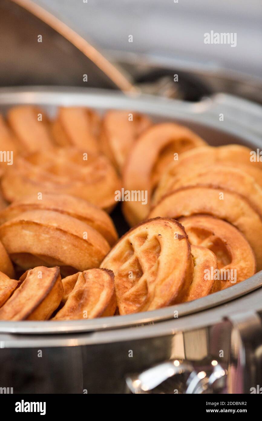 Chafing dish full of small round Belgian waffles.  Many waffles in silver dish, shallow depth of focus in this vertical color photograph. Stock Photo