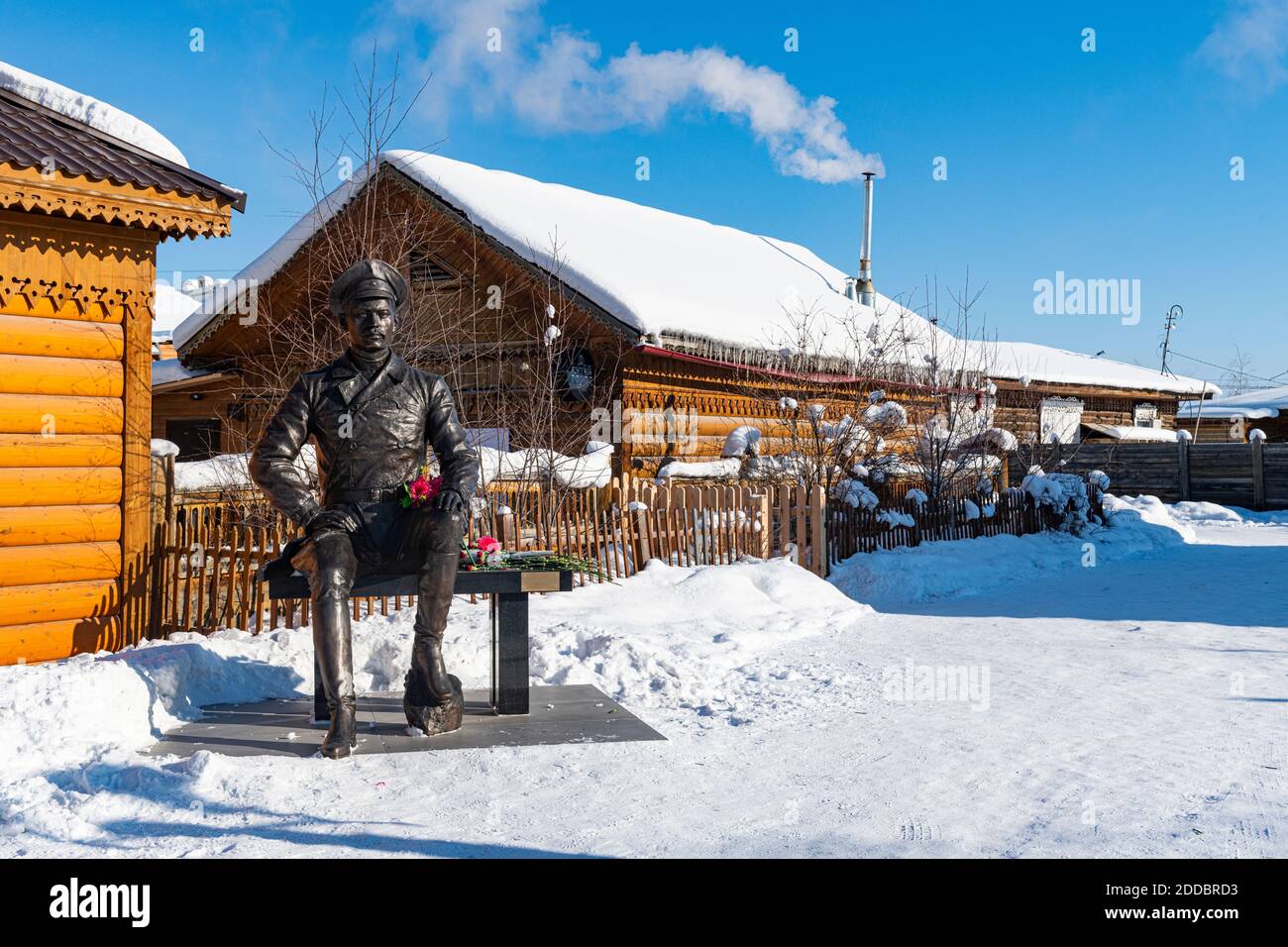 Russia, Republic of Sakha, Yakutsk, Statue of soldier sitting on bench in front of rustic houses in winter Stock Photo