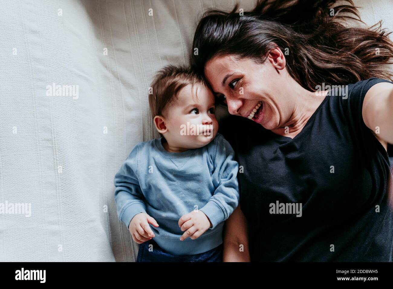 Smiling mother and son taking selfie while lying down on bed at home Stock Photo