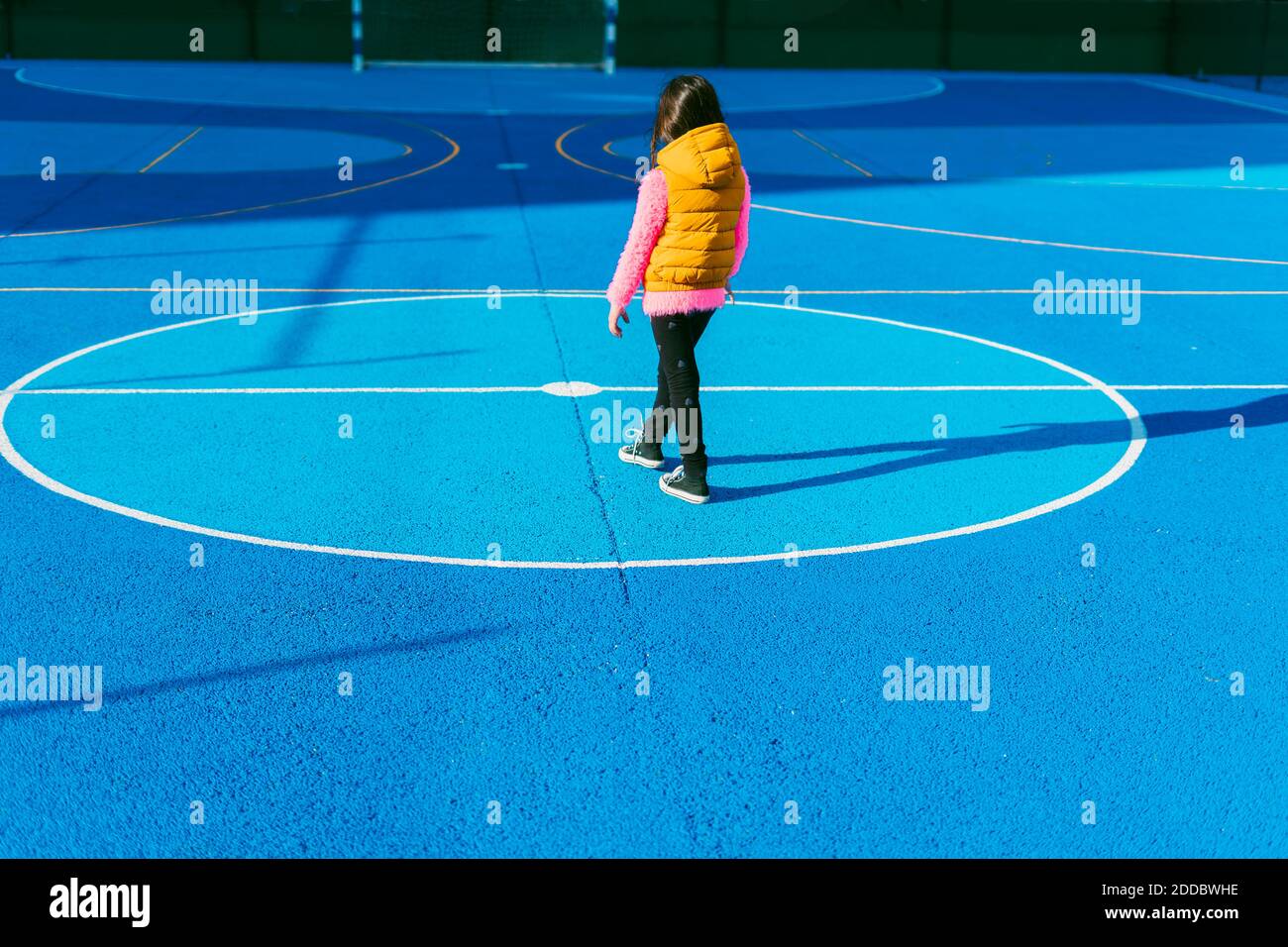 Girl in warm clothing standing on soccer court during sunny day Stock Photo