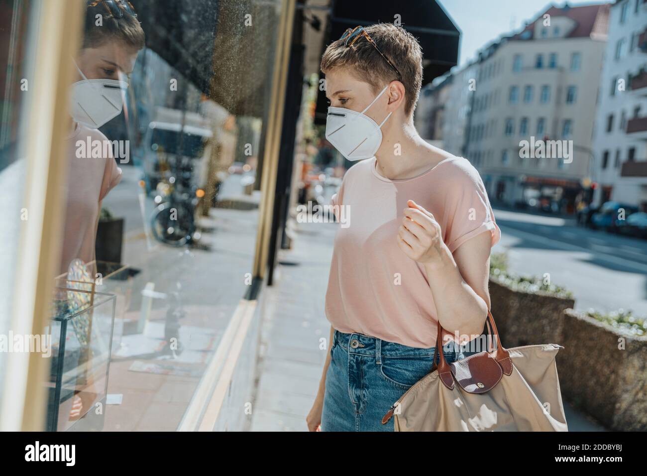 Woman wearing protective face mask doing window shopping while standing on street in city Stock Photo
