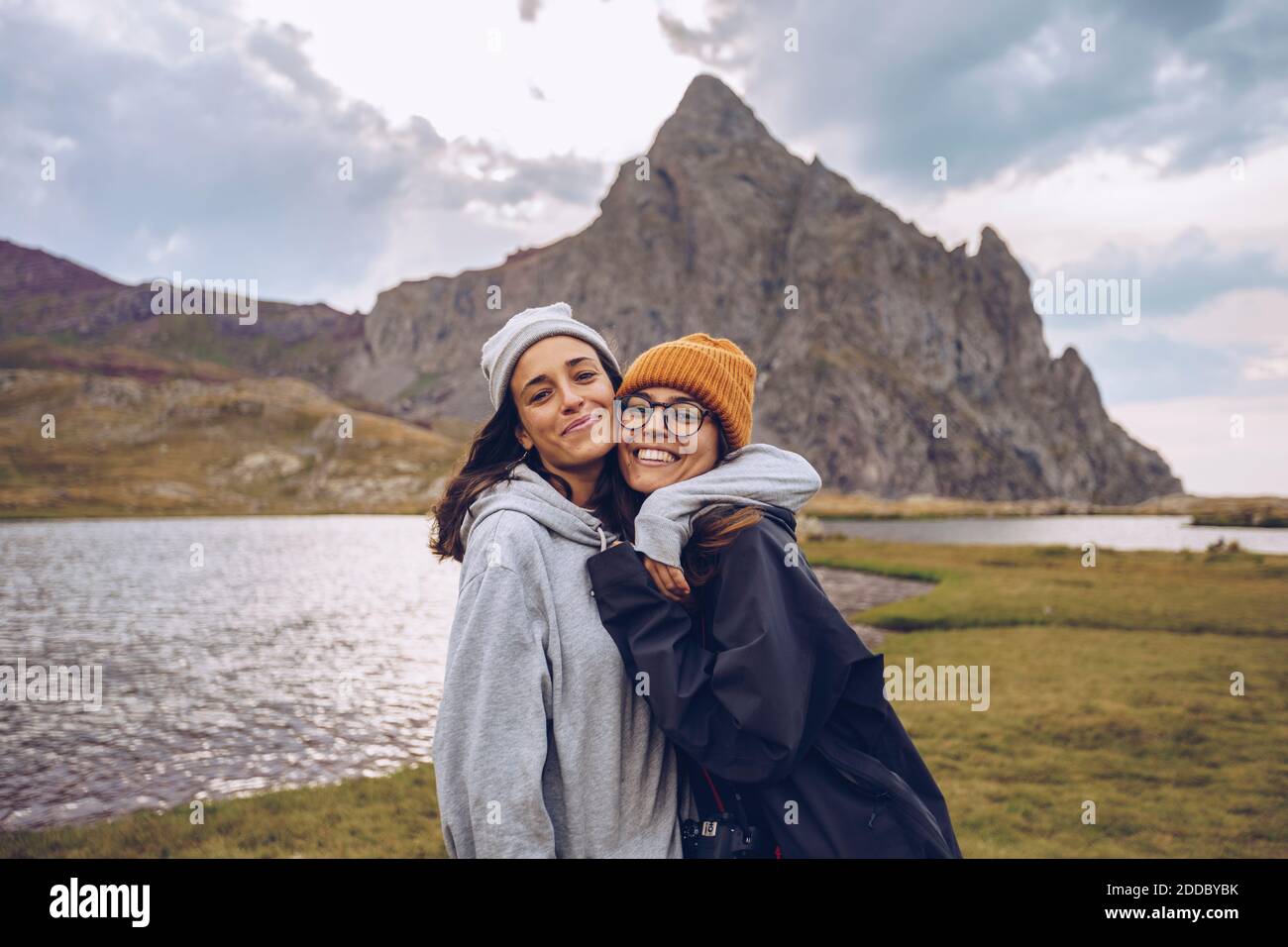 Sisters wearing warm clothing embracing while standing against lake at Ibones of Anayet Stock Photo