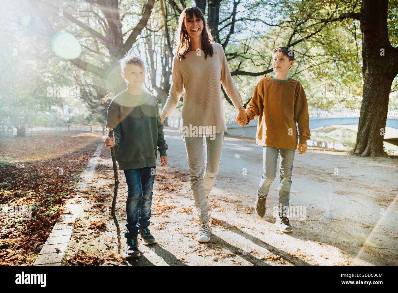 Happy mother and sons walking in public park on sunny day Stock Photo