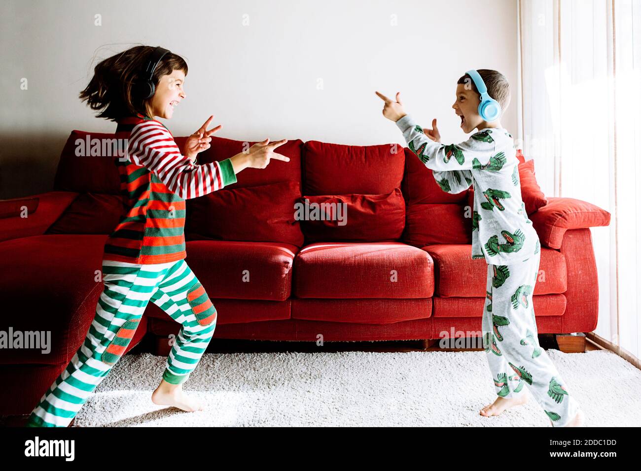 Playful male and female sibling wearing headphones against sofa in living room Stock Photo