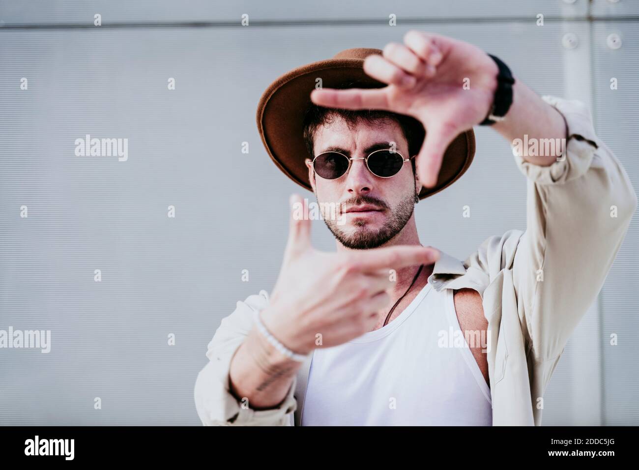 Thoughtful man in hat and sunglasses gesturing against wall Stock Photo