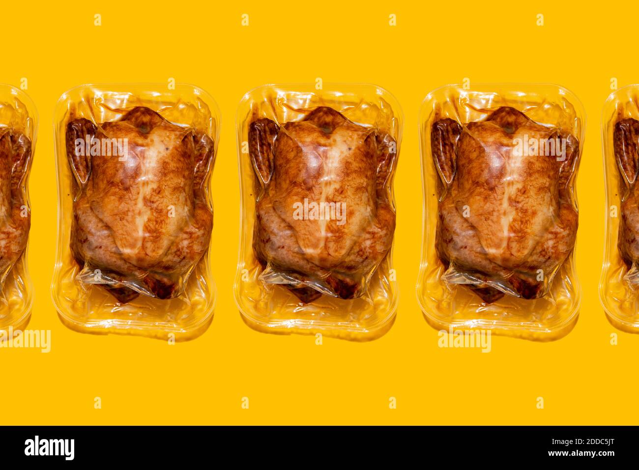 Vacuum packed roasted chickens arranged in a line on yellow background Stock Photo