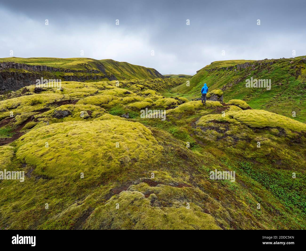 Man exploring green landscape against cloudy sky Stock Photo