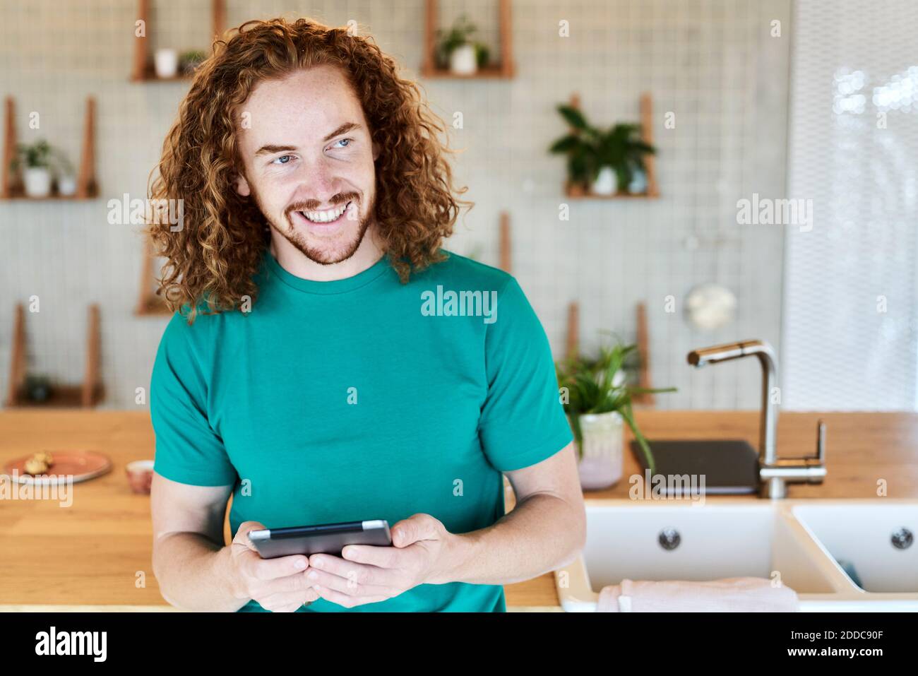Smiling man looking away while using digital tablet in kitchen of studio apartment Stock Photo