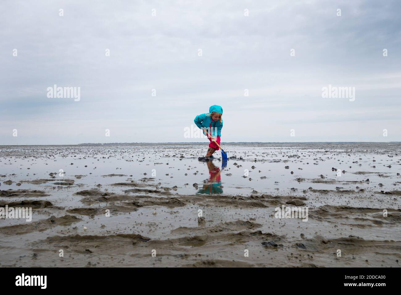 Girl playing in mud flat with shovel against sky at Lower Saxon Wadden Sea National Park, Germany Stock Photo