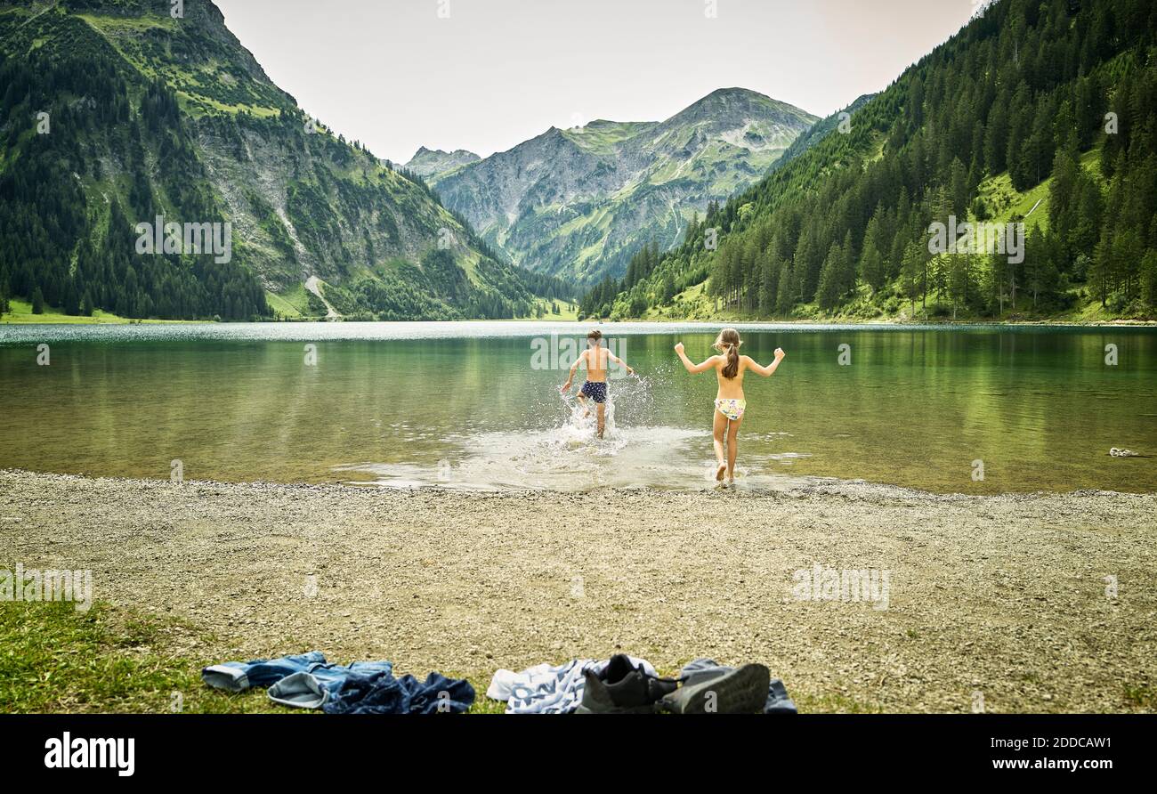 Siblings running at lakeshore while enjoying vacation Stock Photo