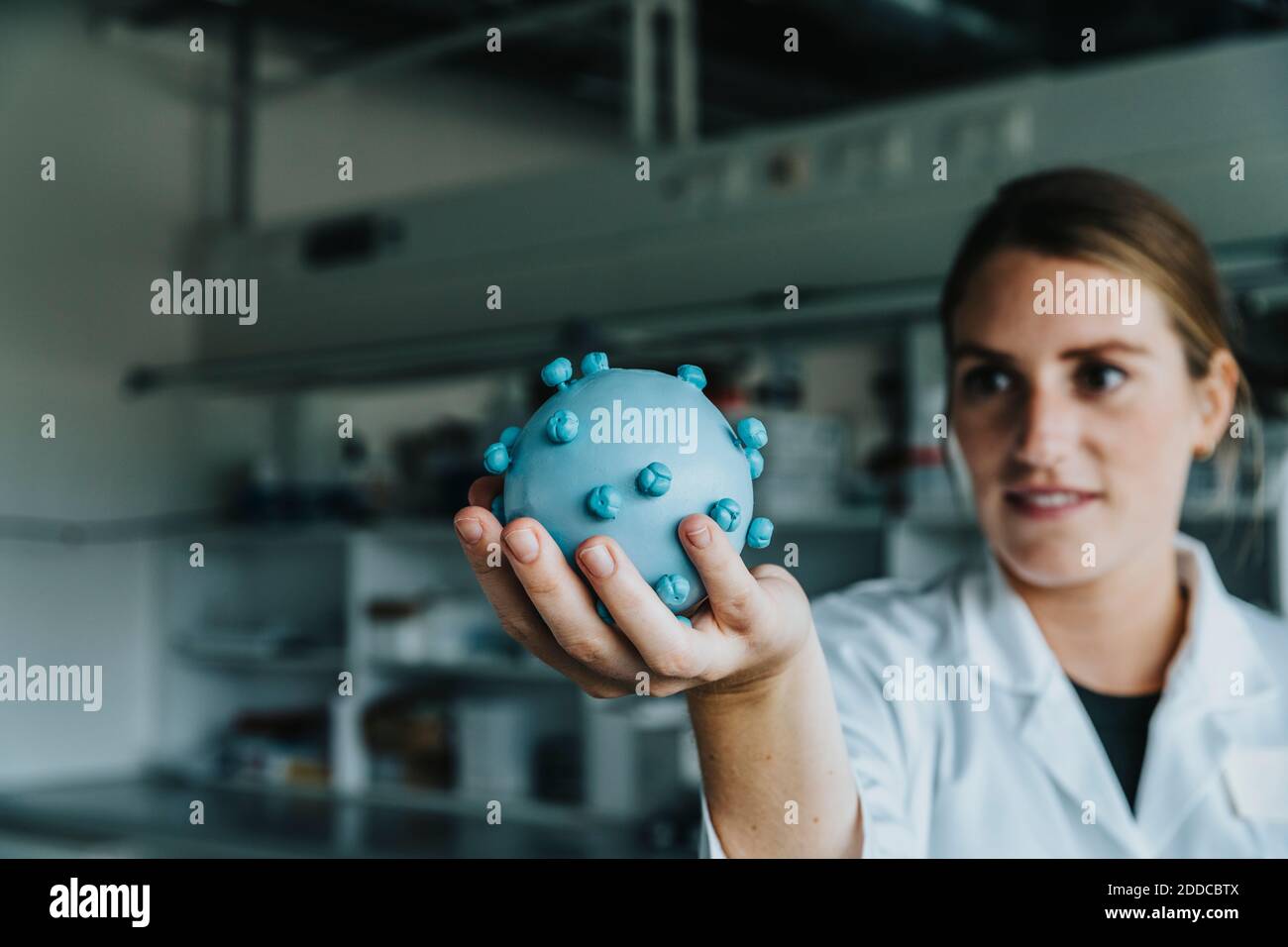 Young scientist holding coronavirus model while standing at laboratory Stock Photo