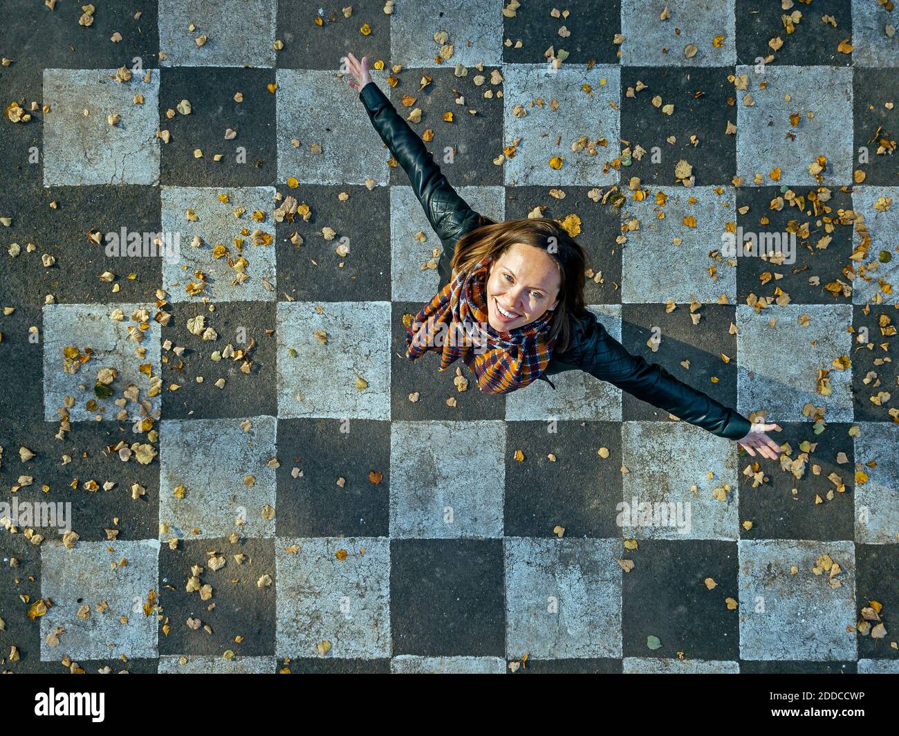 Smiling woman with arms outstretched spinning on asphalt painted with checked pattern Stock Photo