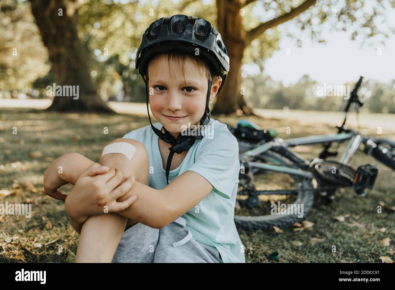 Boy sitting with bandage on knee in pubic park on sunny day Stock Photo