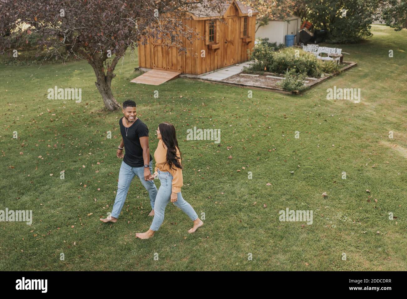 Smiling couple holding hands while walking at backyard Stock Photo - Alamy