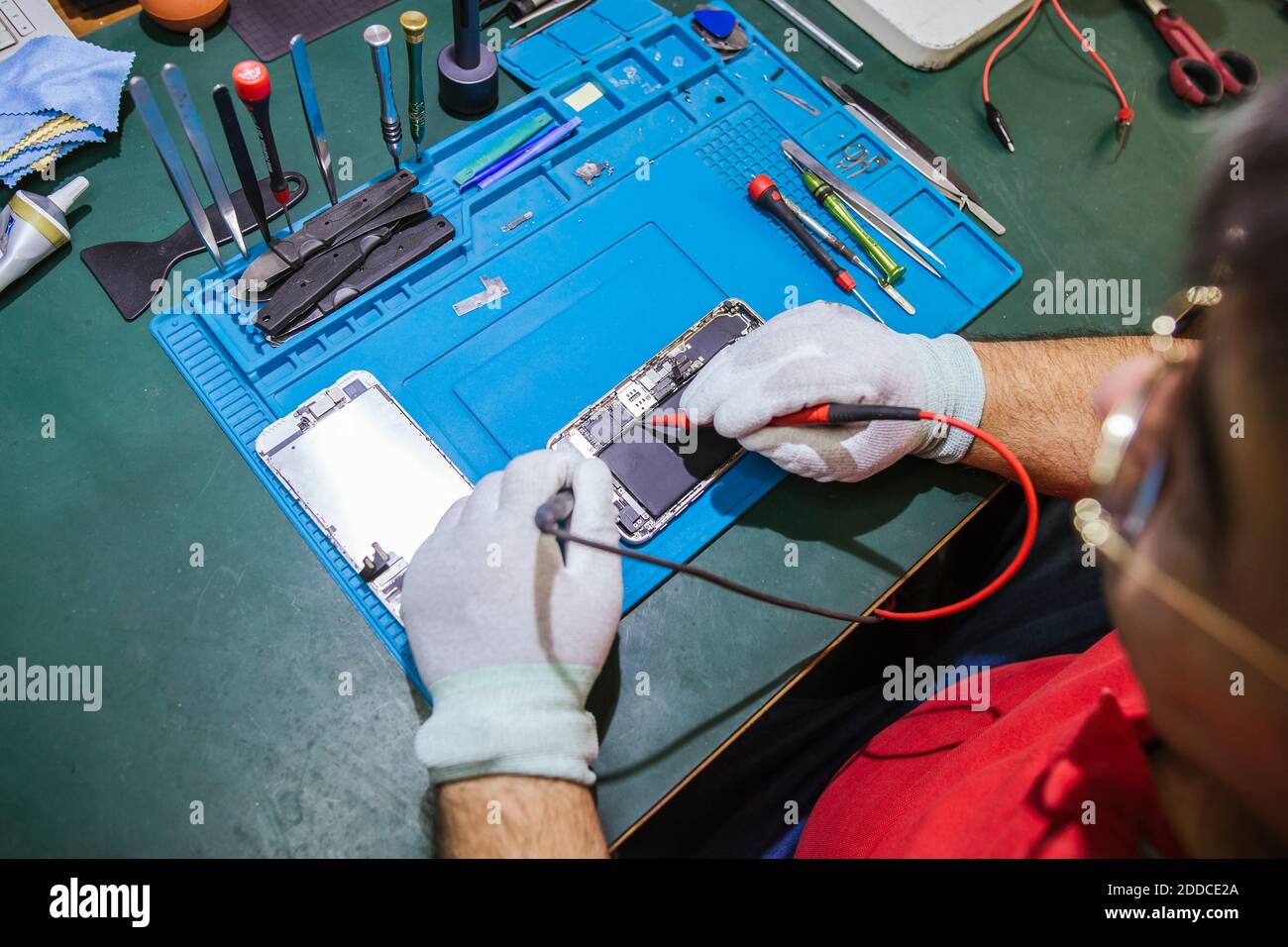 Male engineer examining damaged smart phone at workbench at repair shop Stock Photo