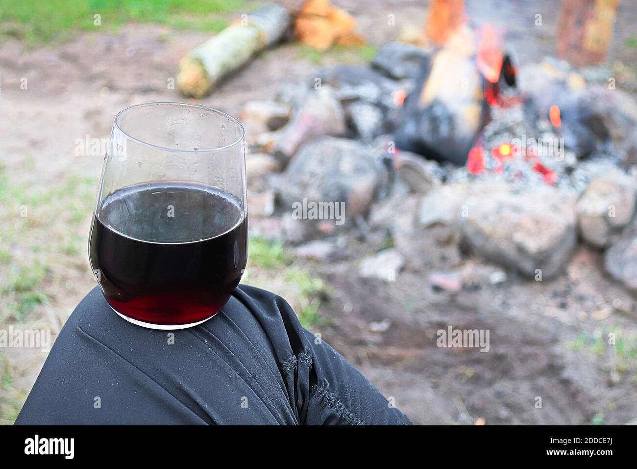 Balancing a glass of wine on a knee against a campfire Stock Photo