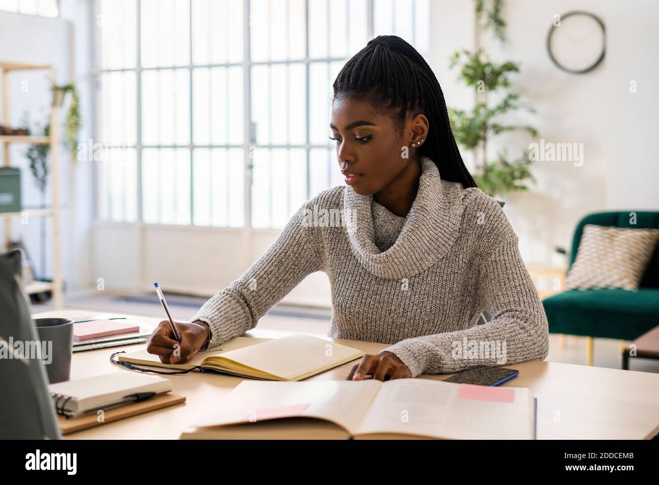 Female student writing in book on table while sitting at home Stock Photo