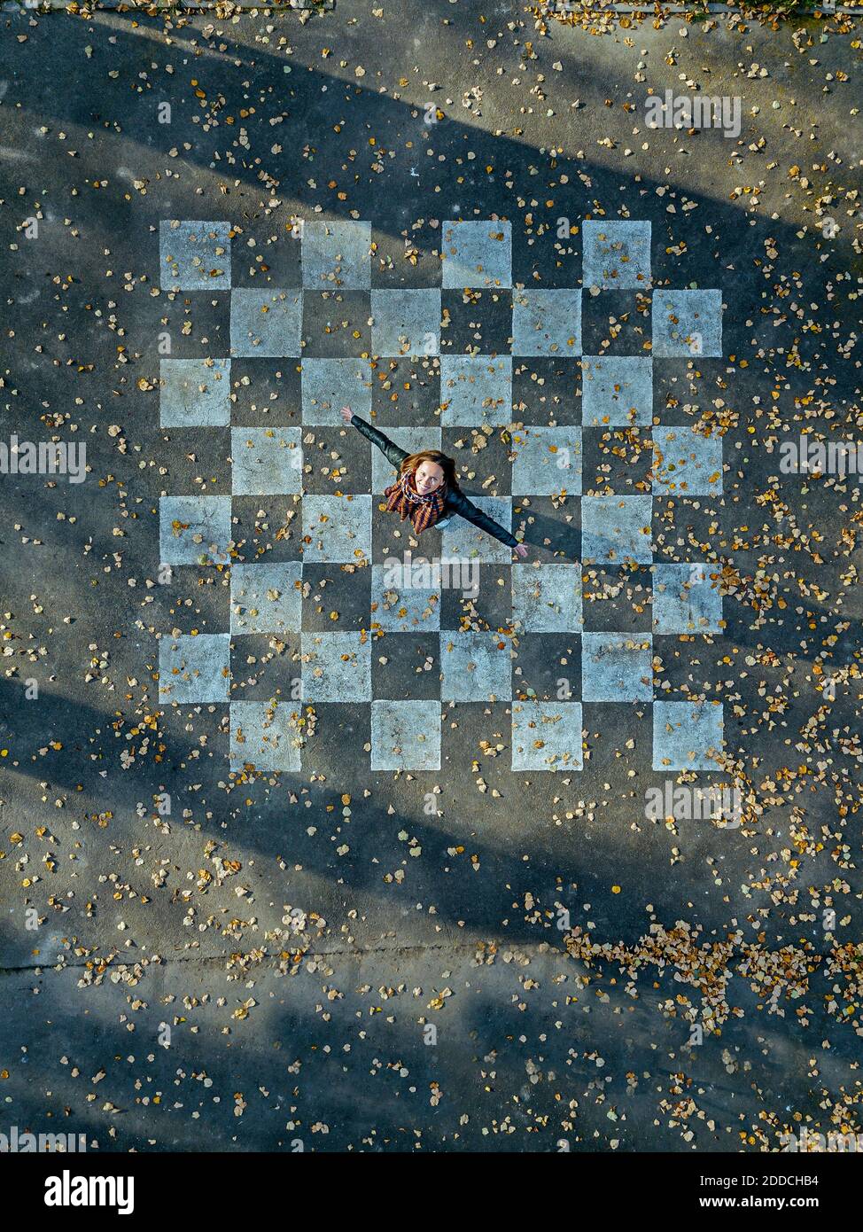Mid adult woman with arms outstretched spinning on asphalt painted with chessboard pattern Stock Photo