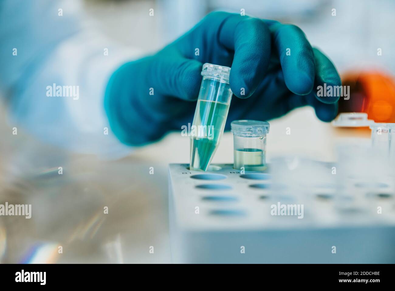 Woman wearing protective glove holding test tube while standing at laboratory Stock Photo