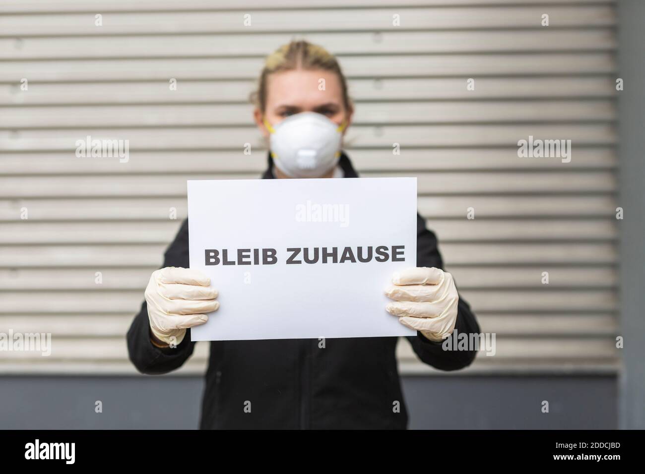 Teenage girl wearing protective mask and gloves holding sign with request 'Bleib Zuhause' Stock Photo