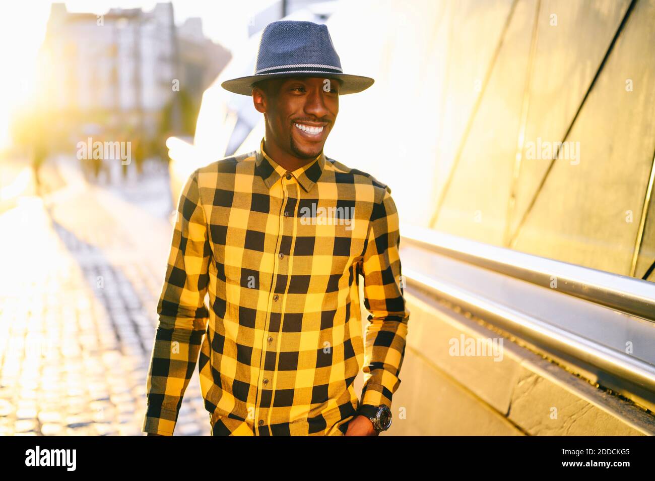Smiling african man in yellow plaid shirt standing in city during sunset Stock Photo