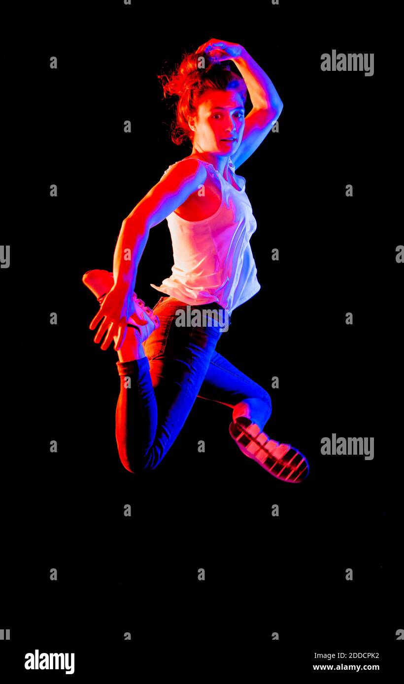 Young woman jumping in mid-air against black background Stock Photo