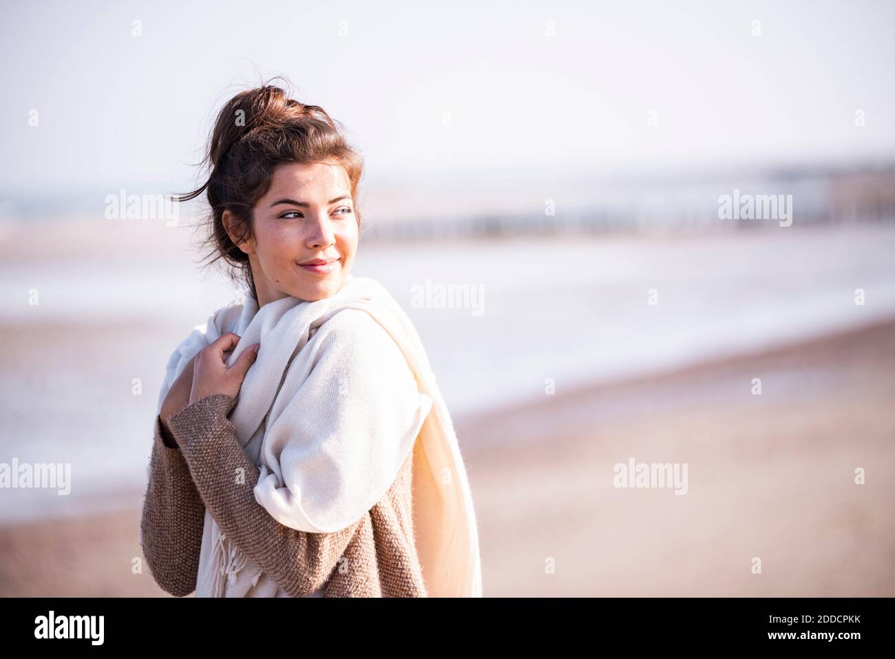 Thoughtful beautiful woman looking away while standing at beach on sunny day Stock Photo