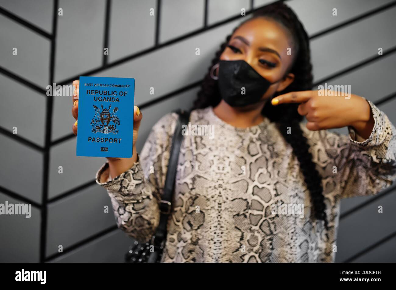 African woman wearing black face mask show Uganda passport in hand. Coronavirus in Africa country, border closure and quarantine, virus outbreak conce Stock Photo