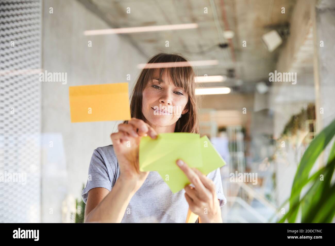 Mature woman sticking adhesive notes on glass material Stock Photo