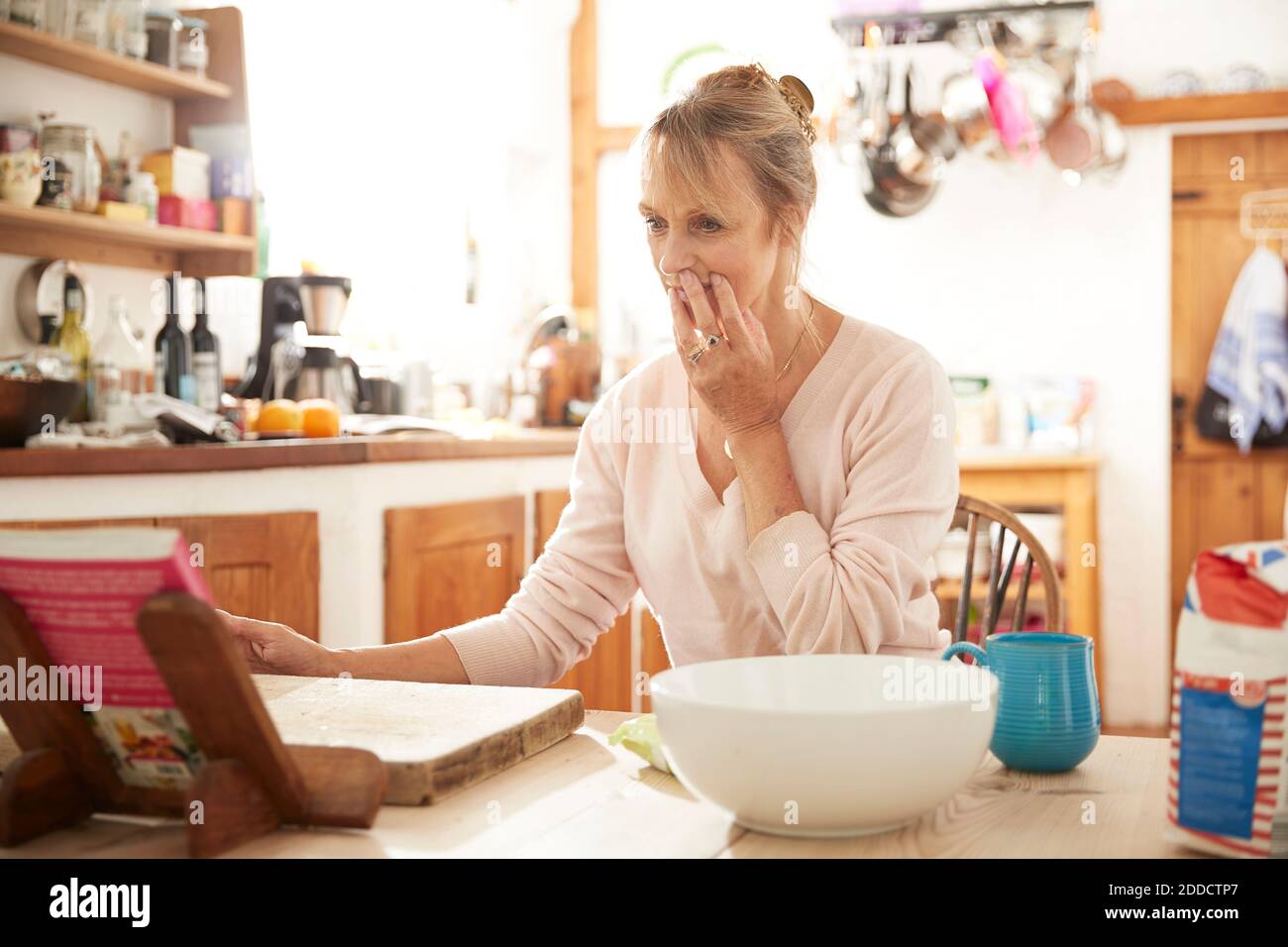 Senior woman reading recipe book while sitting in kitchen Stock Photo