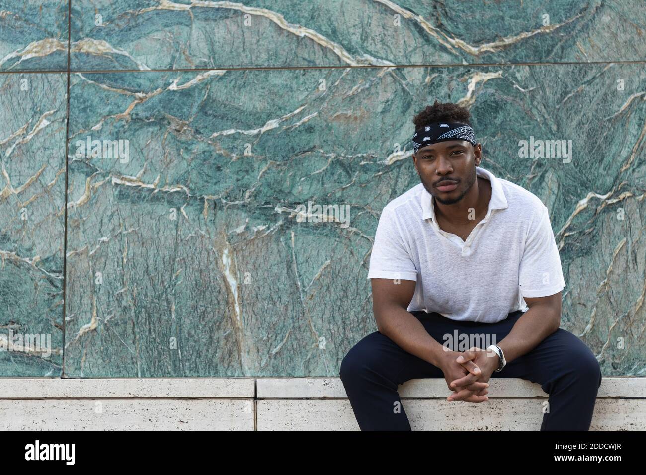 Young man wearing headscarf while sitting against wall Stock Photo